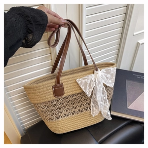Detail der khakifarbenen Strohtasche mit weißer Spitzenschleife und Ledergriffen