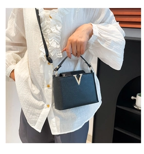 Detail of elegant black crocodile embossed handbag with gold V logo and leather strap