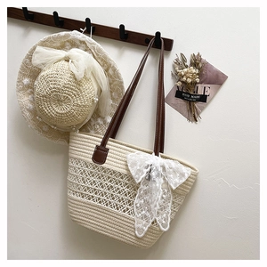 Detail der Strohtasche mit Spitzenschleife und Ledergriffen an einer strukturierten Wand