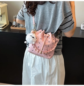 Pink drawstring bucket bag with textured pattern and plush ball detail worn by model