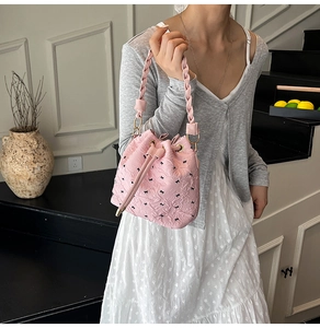 Detail of pink drawstring bucket bag with black bow patterns and woven handle