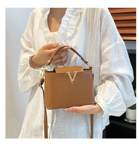 Detail of caramel brown bucket bag with gold V-decoration and white ruffle shirt