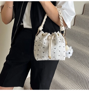 Close-up of white pleated hobo bag with black bow print and fluffy charm pendant