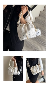 Detail of white pleated bucket bag featuring black bow prints and a plush pompom charm