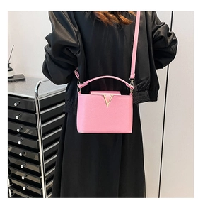 Detailed side view of pink crossbody bag with golden V-shaped logo and leather texture