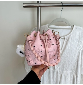 Close-up of pink pleated bucket bag with black bow print and plush charm detail