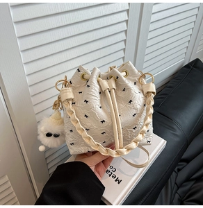 Detail of white pleated bucket bag with floral bow pattern and plush bear charm accessory