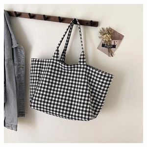 Detail of a black and white gingham canvas tote bag hanging on a minimalist wooden hook