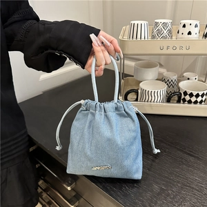 Secchiello minimalista in denim azzurro con coulisse e logo in metallo sul tavolo