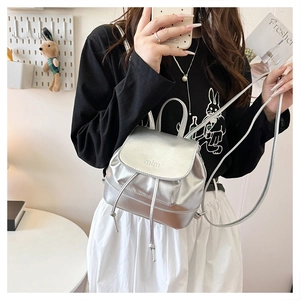 Side view of woman wearing a silver mini backpack with drawstring and embossed mlm flap