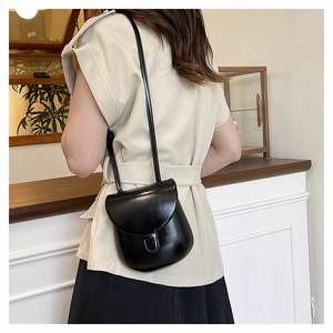 Detail view of a compact black crossbody bag with a glossy finish and minimalist buckle