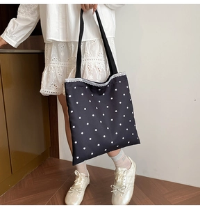 Detailed view of floral pattern embroidery and lace trim on a black canvas tote bag