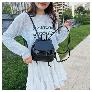 Outdoor shot showing a mini black glossy drawstring backpack worn on a model's back