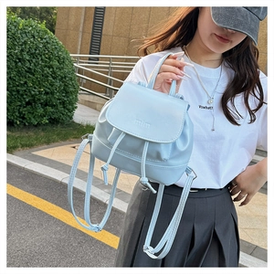 Detail of light blue pleated backpack showing mim logo and drawstring closure in outdoor setting