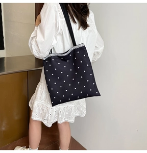 Detail of black canvas tote bag with white floral pattern and lace trim on shoulder