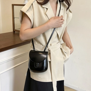 Glossy black crossbody bag with semi-circular flap shown in a cozy indoor setting