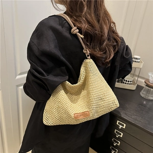Handwoven straw tote bag with brown leather shoulder strap and fashion label detail