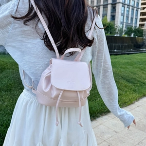 Pink minimalist PU leather backpack with drawstring and flap closure on a model outdoors