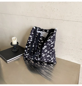 Close-up of black floral canvas tote bag with white flower patterns on a grey surface