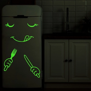 Luminous green cartoon facial expression stickers glowing on a fridge in the dark