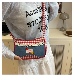 Detail of blue denim and red plaid crossbody bag with lace trim and cherry embroidery