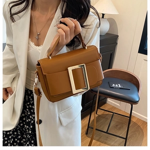 Detail of a brown leather handbag with a large gold square buckle and adjustable strap