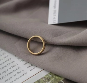 Close-up of a minimalist golden matte finish stainless steel ring on textured fabric