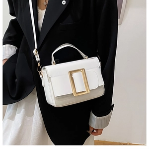 Close-up of white leather handbag featuring a large gold square metal buckle and strap
