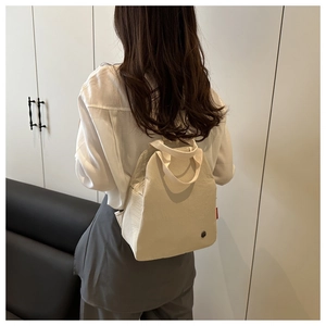 Detail view of a cream canvas mini backpack with a red label and woven top handle