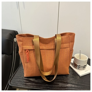 Detail van terracotta geweven draagtas met ritsvak en kaki nylon riem op houten tafel