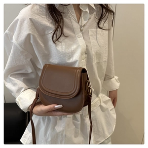 Close-up of a brown saddle bag featuring smooth PU leather and gold metal hardware detail