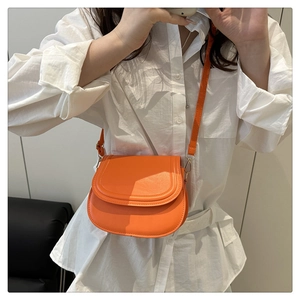 Mirror selfie showing a vibrant orange faux leather saddle bag with a long shoulder strap