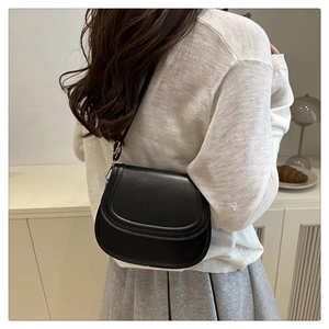 Side view of a black minimalist saddle bag on a model wearing a pleated skirt