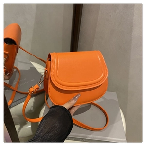 Detailed shot of bright orange PU leather saddle bag with gold metal hooks and stitching