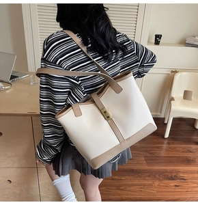 Model wearing a large contrast color tote bag with metallic buckle and slim shoulder straps