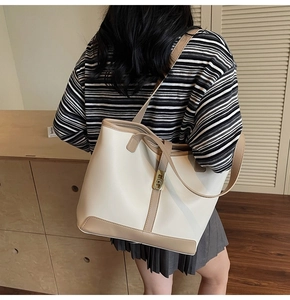 Detail view of large bi-color tote bag with golden buckle on a model shoulder