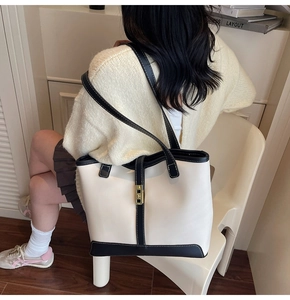 Detail of minimalist tote bag with contrast piping and gold buckle on a model shoulder