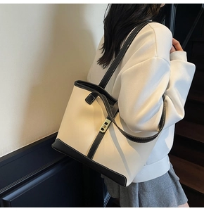 Detail of a contrast color tote bag featuring white leather and black trim with gold lock