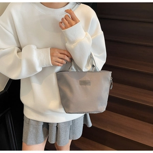 Détail du sac à main gris en nylon lustré avec étiquette FASHION sur escalier en bois