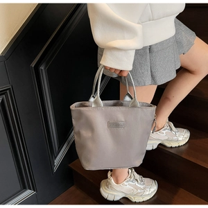 Detailed close-up of a grey nylon tote bag featuring a stitched fashion label on the front