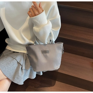 Close-up of a grey waterproof nylon handbag with a FASHION label held by a model