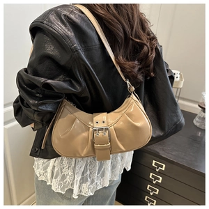 Detail of beige pleated crescent bag with oversized metal buckle and glossy finish