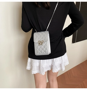 Close-up of silver quilted mobile phone bag featuring a golden bow buckle and chain strap