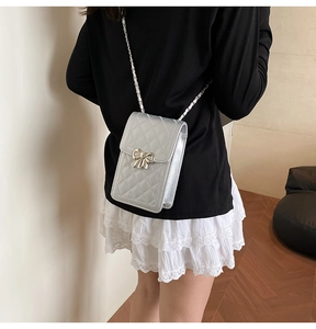 Detail of silver quilted crossbody phone bag with metal bow accent and chain strap