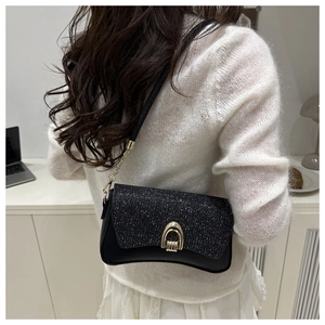 Detail of black sequin crossbody bag with gold U-shaped buckle on a model in an office