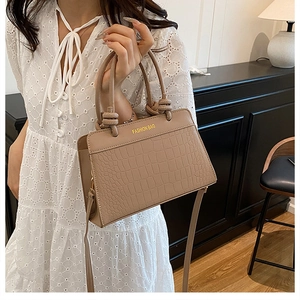 Detail of apricot crocodile-patterned bag featuring a knot handle and gold lettering
