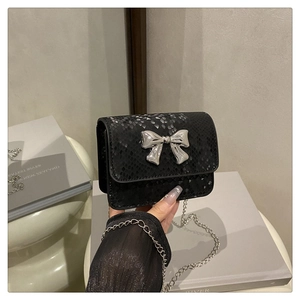 Detalle de mini bolso negro con textura de serpiente y hebilla de lazo plateado