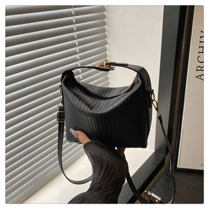 Détail d'un sac bandoulière noir plissé avec finitions dorées et texture chic