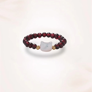 Detail of beaded ring with deep red stones and a white cat-shaped natural stone charm