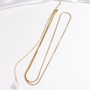 Flat lay of a layered gold snake chain necklace featuring a white baroque pearl pendant